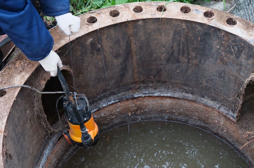 worker lowering a pump into an open cesspool for emptying